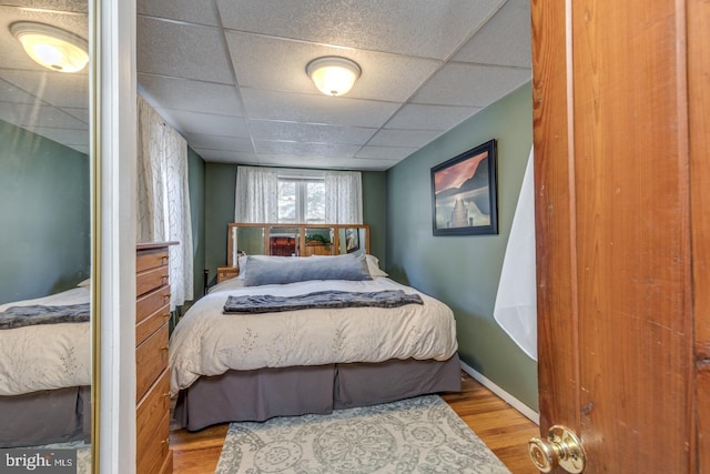 bedroom featuring a drop ceiling, baseboards, and wood finished floors