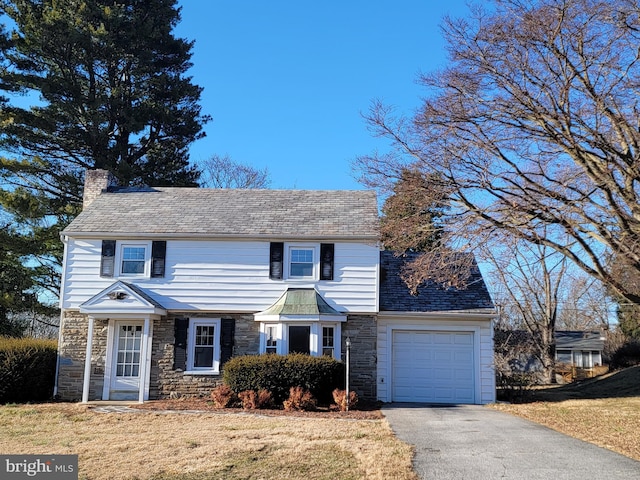 view of front of property featuring driveway, stone siding, a chimney, an attached garage, and a front lawn