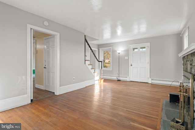 entryway with baseboards, a baseboard radiator, wood finished floors, stairs, and a fireplace