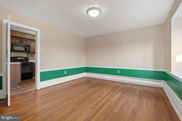 empty room with a baseboard heating unit, light wood-type flooring, and baseboards