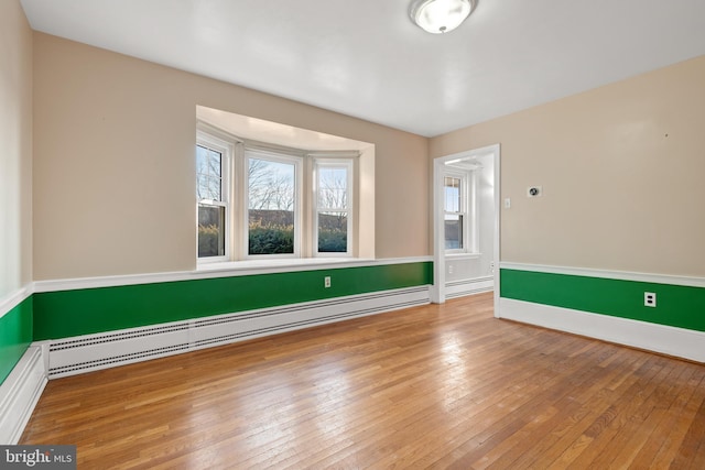 empty room with a baseboard radiator, baseboards, and wood-type flooring