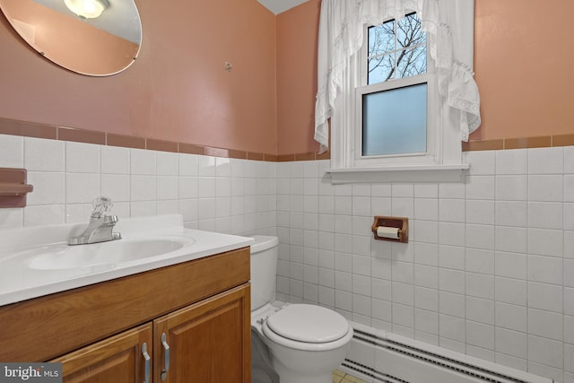 bathroom featuring toilet, a baseboard heating unit, vanity, tile walls, and wainscoting