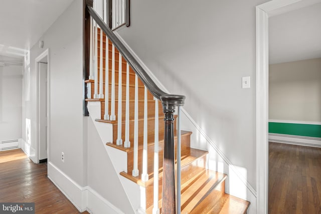 stairway featuring wood-type flooring, a baseboard heating unit, and baseboards