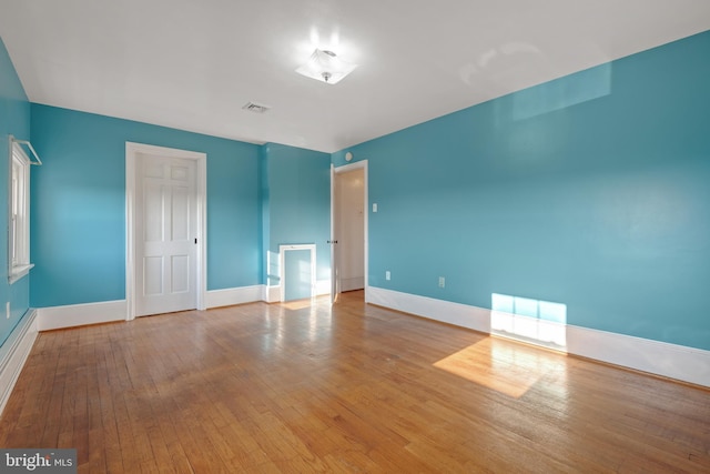 empty room with hardwood / wood-style flooring, baseboards, and visible vents