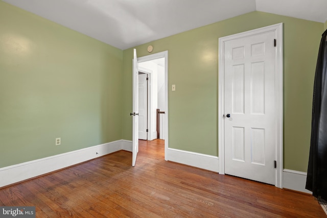 unfurnished bedroom featuring lofted ceiling, baseboards, and wood finished floors