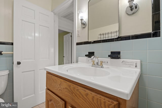 half bath with toilet, vanity, tile walls, and tile patterned floors