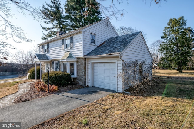 traditional-style house with an attached garage, stone siding, a chimney, and aphalt driveway