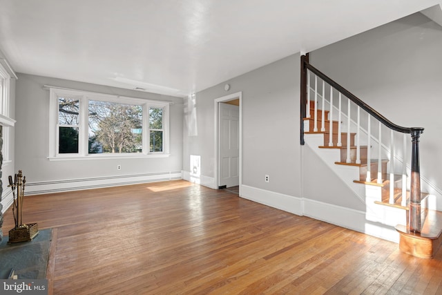 unfurnished living room featuring a baseboard heating unit, wood-type flooring, stairs, and baseboards