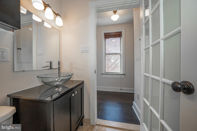 half bathroom featuring toilet, baseboards, wood finished floors, and vanity