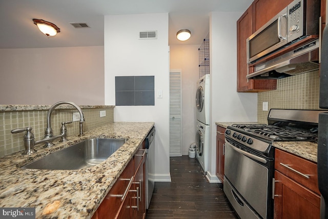 kitchen with stainless steel appliances, visible vents, dark wood-type flooring, stacked washer / dryer, and a sink