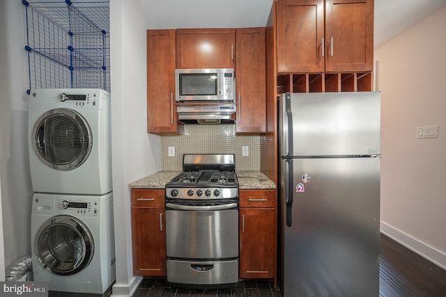 kitchen with light stone counters, stacked washer and clothes dryer, decorative backsplash, appliances with stainless steel finishes, and wall chimney range hood