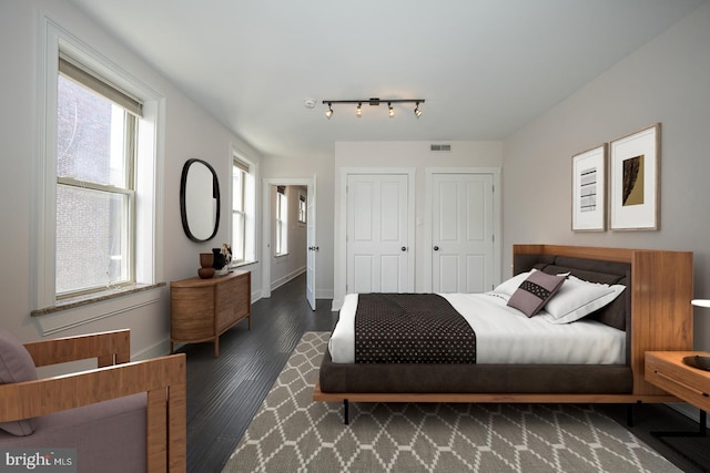 bedroom with visible vents, two closets, baseboards, and wood finished floors