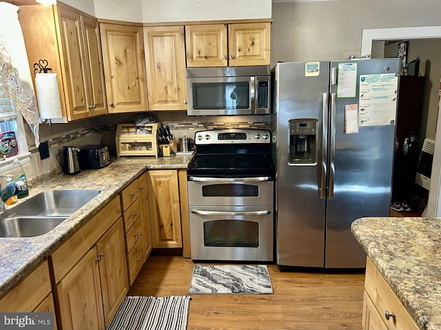 kitchen with light wood finished floors, decorative backsplash, stainless steel appliances, and a sink