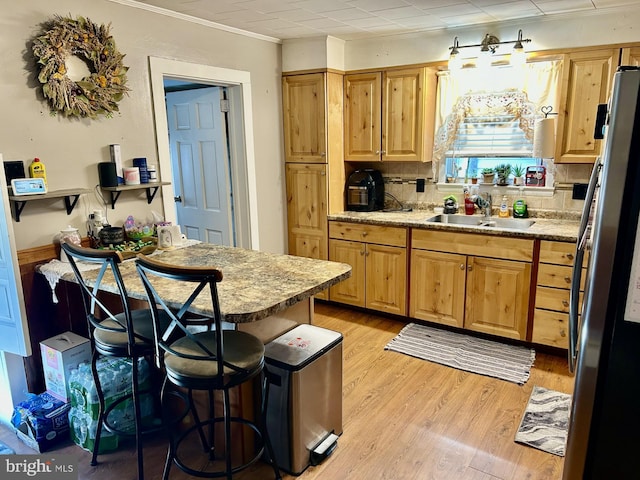 kitchen with tasteful backsplash, freestanding refrigerator, light countertops, light wood-type flooring, and a sink