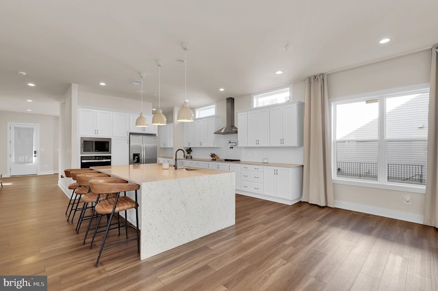 kitchen with wall chimney range hood, recessed lighting, light wood-style floors, and stainless steel appliances