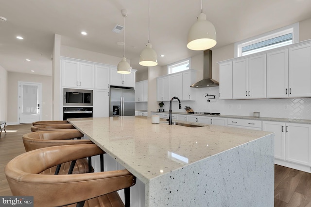 kitchen featuring visible vents, a sink, appliances with stainless steel finishes, wall chimney range hood, and backsplash