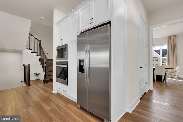 kitchen with light wood finished floors, white cabinets, and appliances with stainless steel finishes