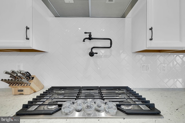 room details with light stone counters, decorative backsplash, white cabinets, and stainless steel gas cooktop