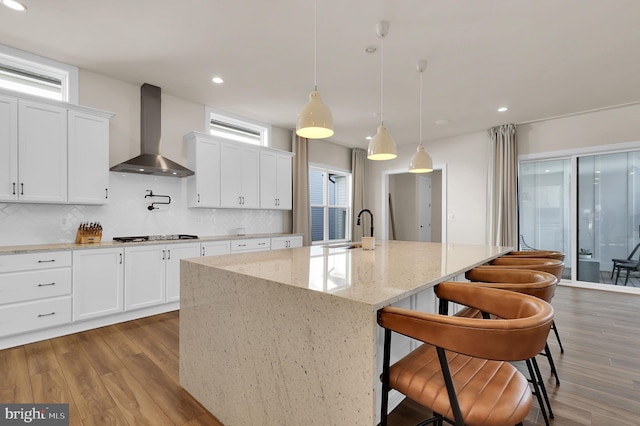 kitchen with decorative backsplash, wall chimney range hood, wood finished floors, and a sink