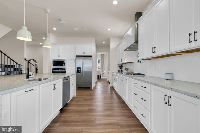 kitchen with wood finished floors, a sink, stainless steel appliances, white cabinetry, and wall chimney range hood