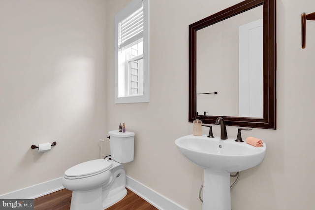 half bathroom with toilet, wood finished floors, baseboards, and a sink