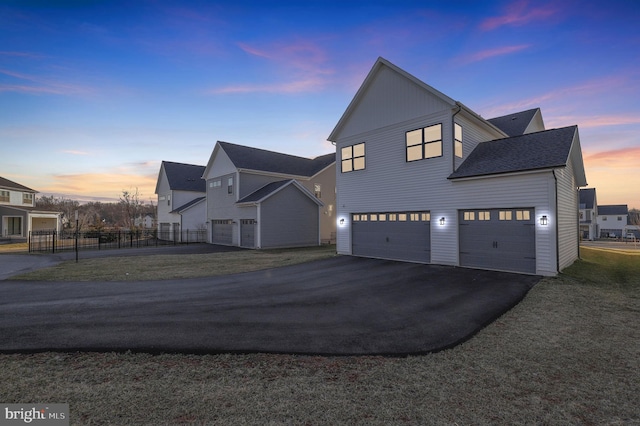 property exterior at dusk featuring driveway, fence, a yard, board and batten siding, and an attached garage