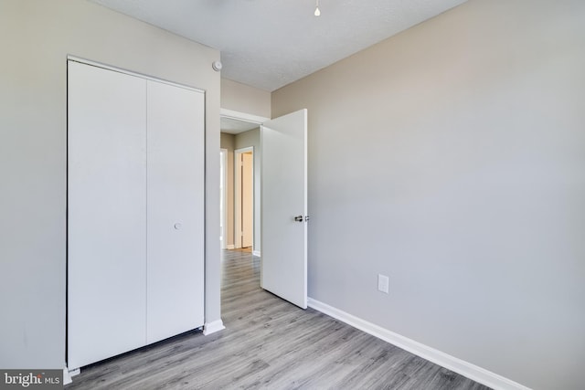 unfurnished bedroom with light wood-type flooring, a closet, a textured ceiling, and baseboards