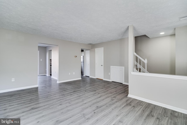 empty room featuring stairs, a textured ceiling, baseboards, and wood finished floors