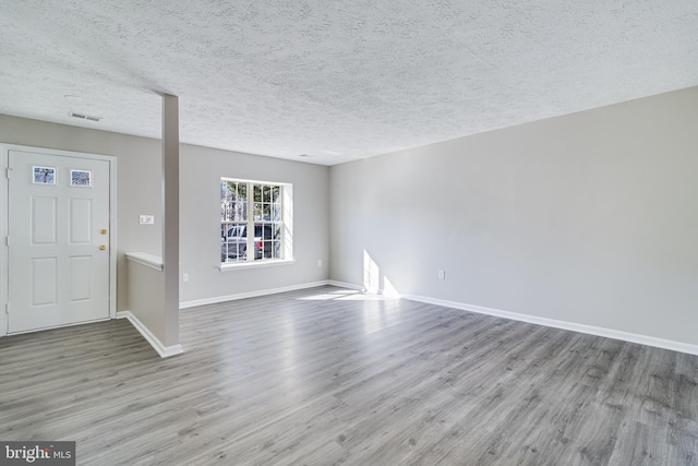 unfurnished living room featuring a textured ceiling, wood finished floors, visible vents, and baseboards