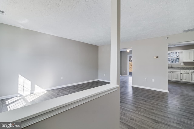 unfurnished room with dark wood-style flooring, visible vents, a textured ceiling, and baseboards