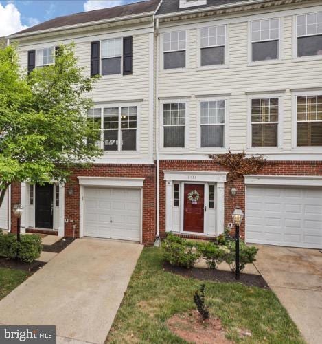 townhome / multi-family property with brick siding, an attached garage, and driveway