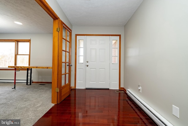 foyer entrance with baseboard heating, a baseboard heating unit, a textured ceiling, wood finished floors, and baseboards