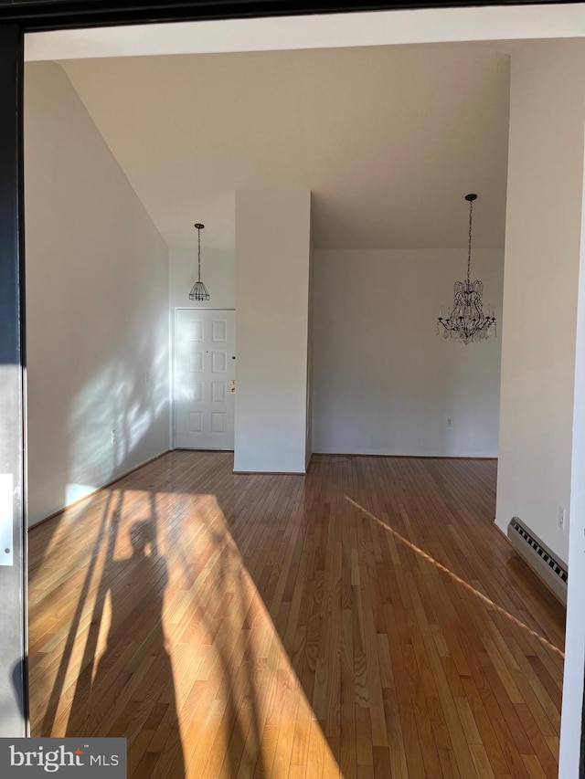 unfurnished room with hardwood / wood-style floors, baseboard heating, and an inviting chandelier