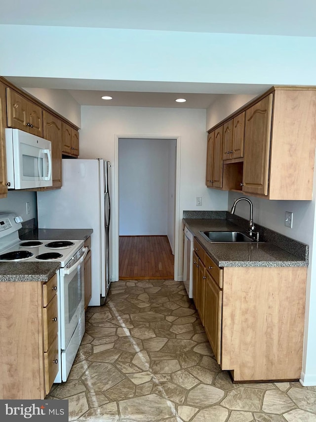 kitchen with dark countertops, recessed lighting, stone finish flooring, a sink, and white appliances