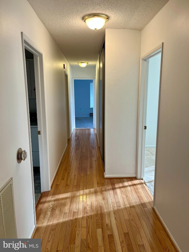 hallway with hardwood / wood-style flooring, baseboards, visible vents, and a textured ceiling