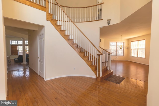 stairway with baseboards, a high ceiling, an inviting chandelier, and hardwood / wood-style flooring