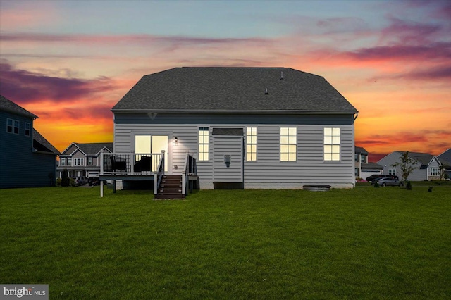 back of house at dusk featuring a shingled roof, a lawn, and a wooden deck