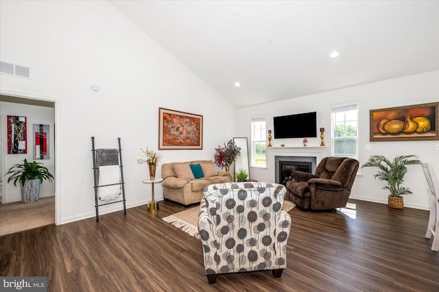 living area with baseboards, visible vents, a glass covered fireplace, dark wood-style floors, and high vaulted ceiling