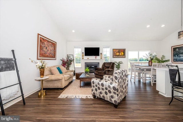 living area with vaulted ceiling, a glass covered fireplace, dark wood-style floors, and recessed lighting