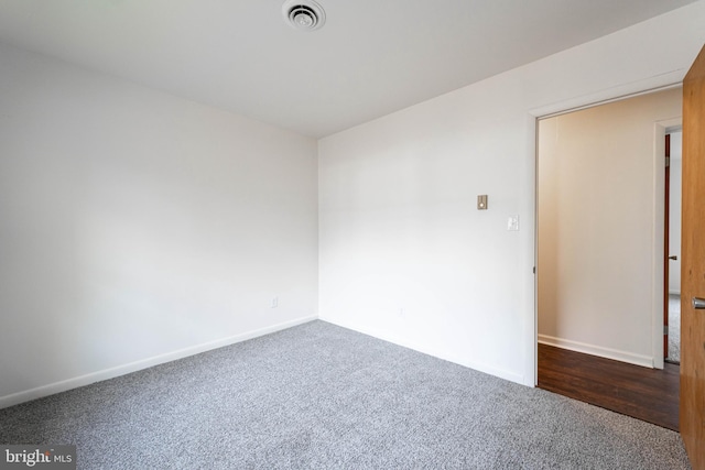 unfurnished room featuring visible vents, dark carpet, and baseboards