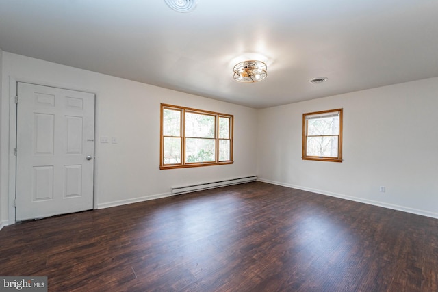 unfurnished room with visible vents, a baseboard heating unit, dark wood-style flooring, and a wealth of natural light