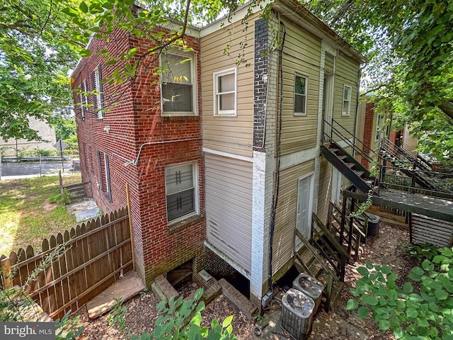 view of home's exterior with central AC, brick siding, and fence