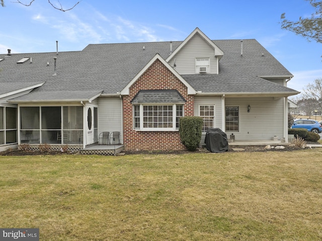 rear view of property with a sunroom, roof with shingles, a lawn, and brick siding