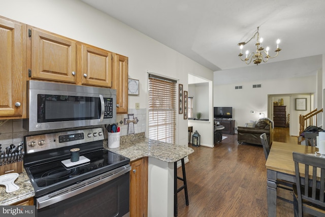 kitchen featuring a notable chandelier, stainless steel appliances, open floor plan, light stone countertops, and dark wood-style floors