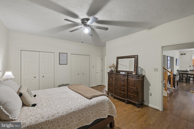 bedroom featuring wood finished floors, a ceiling fan, baseboards, visible vents, and multiple closets