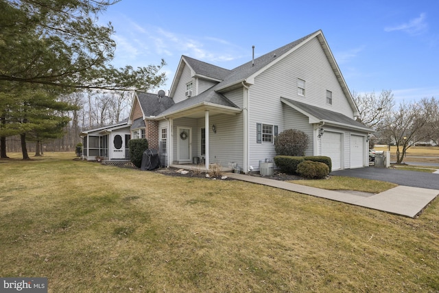 view of front of home with an attached garage, a shingled roof, a sunroom, driveway, and a front yard