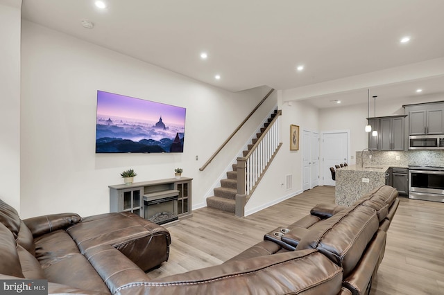 living area with stairs, recessed lighting, baseboards, and light wood-style floors