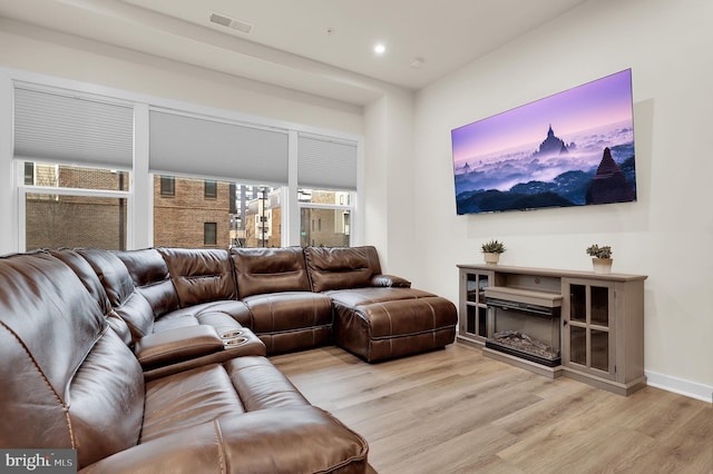 living room featuring light wood finished floors, recessed lighting, visible vents, a glass covered fireplace, and baseboards