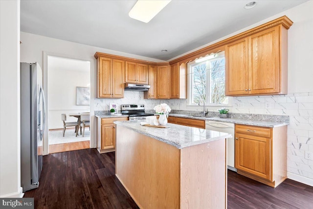 kitchen featuring light stone countertops, dark wood finished floors, a sink, under cabinet range hood, and appliances with stainless steel finishes