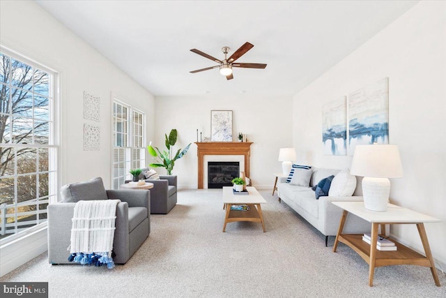 living room with a glass covered fireplace, carpet, baseboards, and ceiling fan